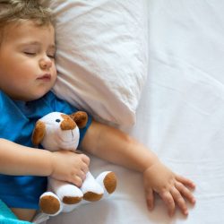 Cute baby boy sleeping on the bed at home with toy. Free space
